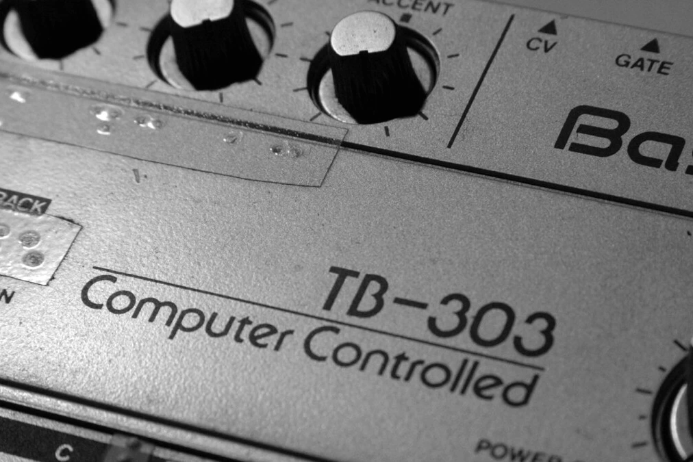 Gros plan d’une TB-303 et de ses clones et émulations, boutons et séquenceur éclairés sur fond sombre