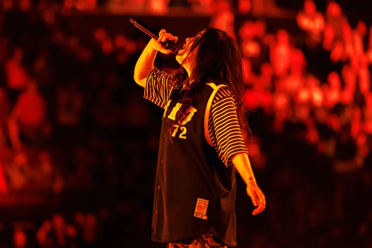 Billie Eilish sur scène, micro à la main, éclairée par des projecteurs bleus lors de la tournée « Hit Me Hard & Soft »
