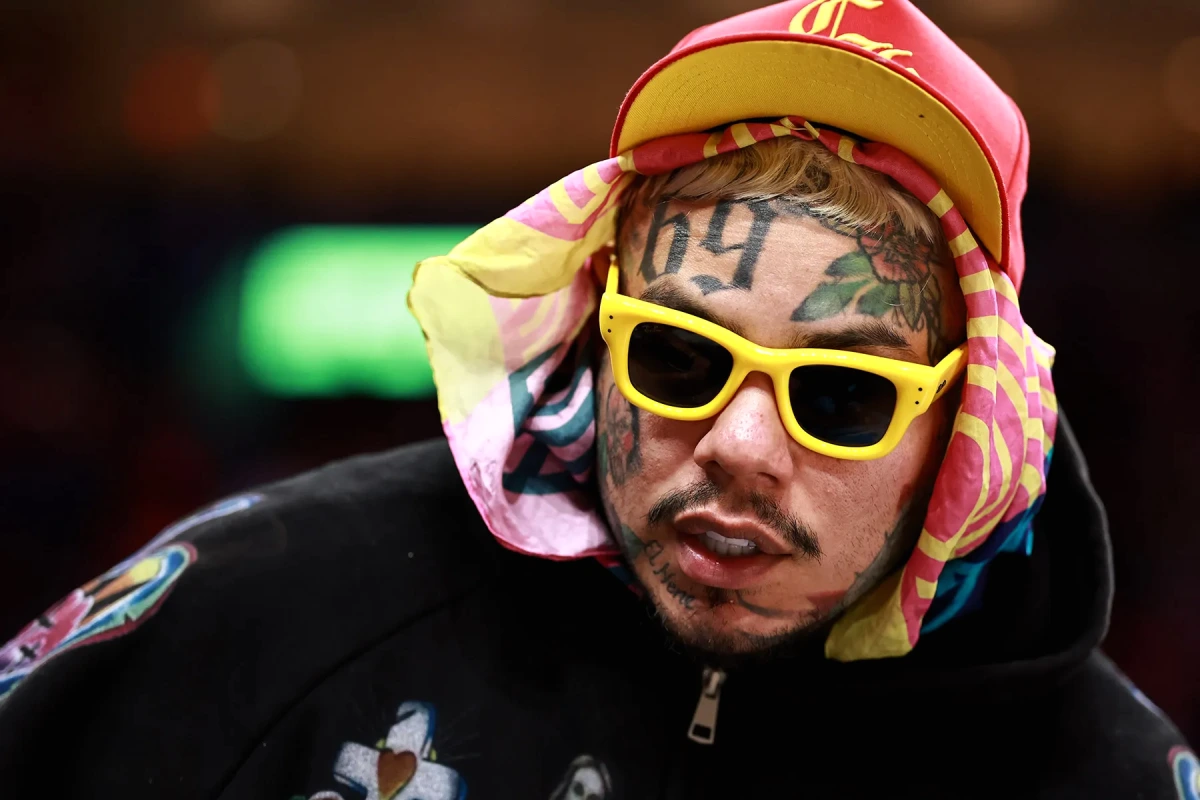 6ix9ine au micro sur scène, cheveux multicolores et tatouages visibles, regard tourné vers le public