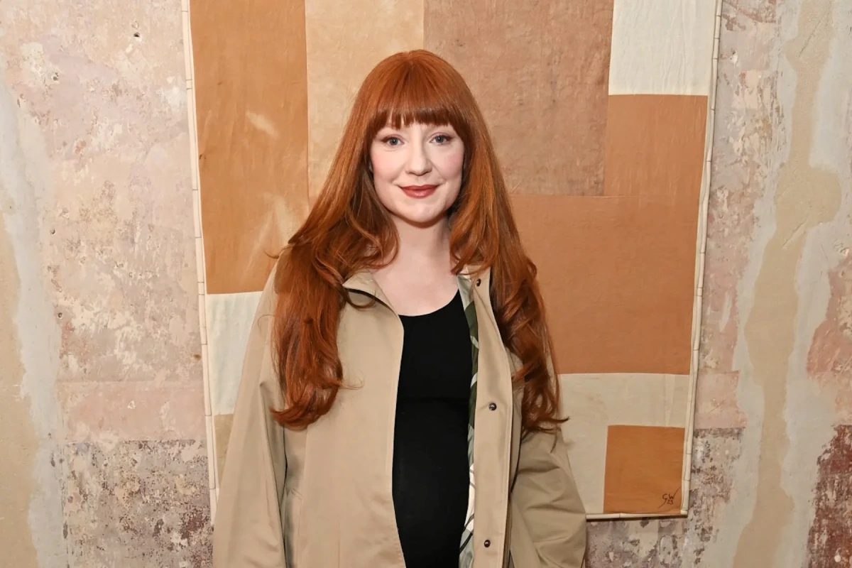Nicola Roberts souriante en portrait, posant devant un fond neutre, cheveux roux et tenue claire.
