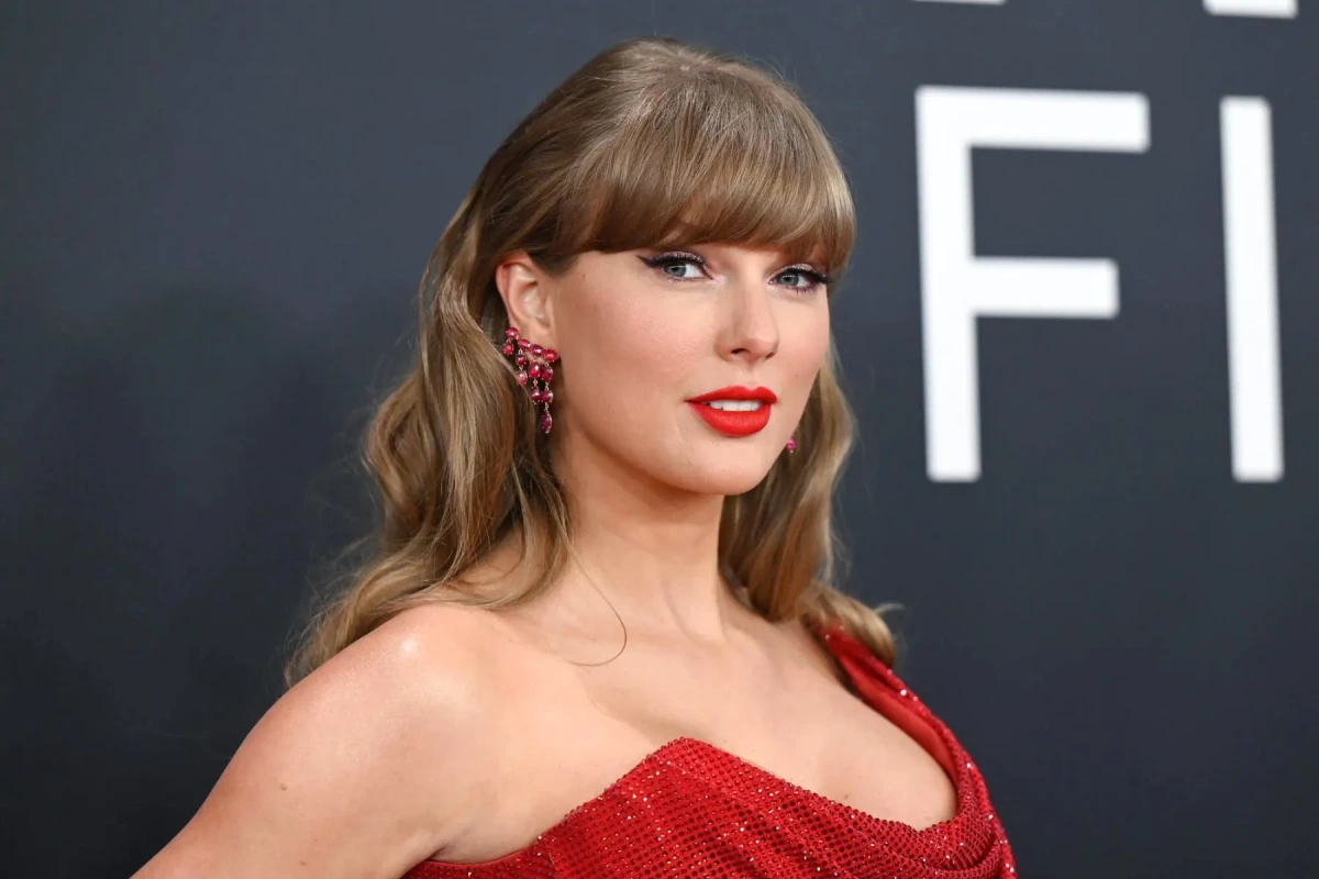 Taylor Swift souriante sur scène, tenant un micro, éclairée par des projecteurs lors d’un concert.