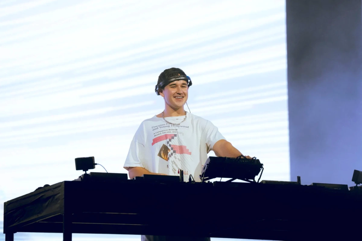 John Summit sur scène à Lollapalooza, micro en main, éclairé par des projecteurs et fumée de scène
