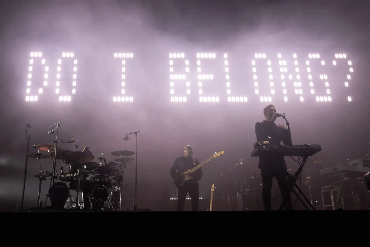 Massive Attack sur scène, éclairages bleus et fumée, devant une foule en concert, micro à la main