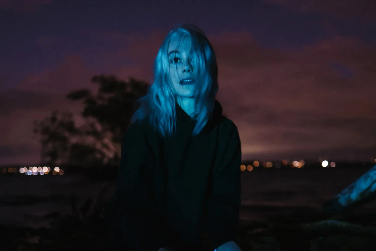 Phoebe Bridgers sur scène, guitare à la main, sous des projecteurs bleus, devant un micro.