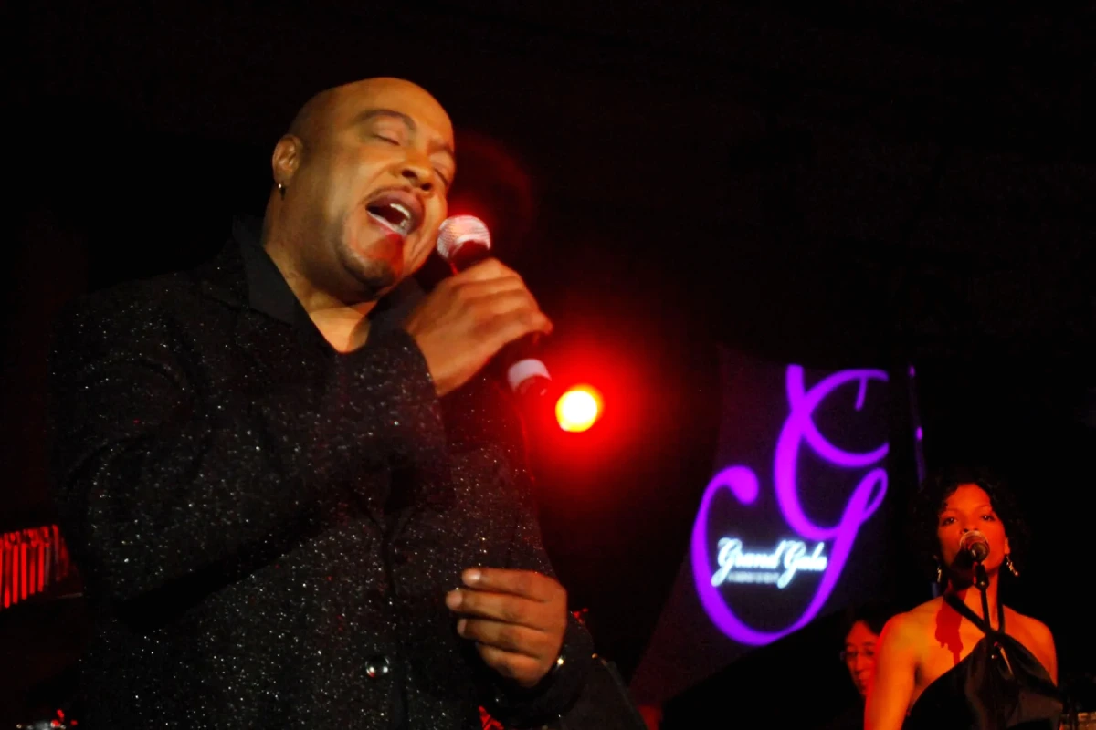 Portrait de Peabo Bryson sur scène, micro en main, sous des projecteurs bleus et violets.